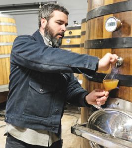 Ryan Burke pouring glass of cider from barrel, at Angry Orchard.