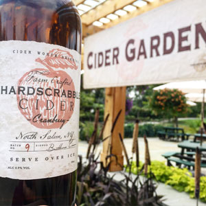 Closeup photo of a bottle from Hardscrabble Cider, with Cider Garden sign in background.