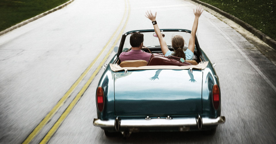 photo of couple in a convertible car, driving down the road