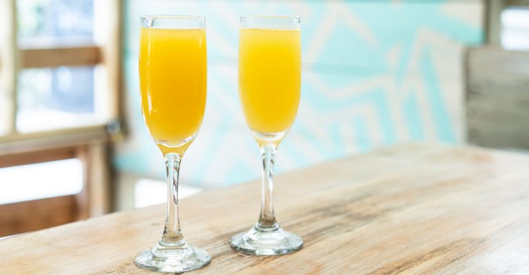 photo of two glasses of mimosas on tabletop.