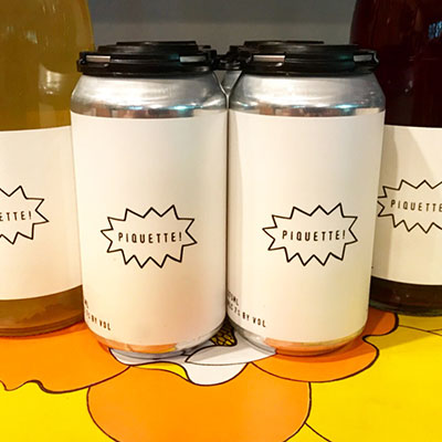 cans of piquette wine from Wild Arc Farms on a bright yellow and orange flowered tablecloth