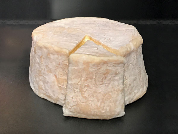 Large round of Gatekeeper cheese with a slice removed, on gray background.