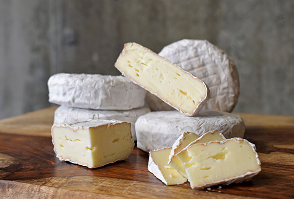 Stacks of Hartwell cheese in rounds and slices on wood tabletop.