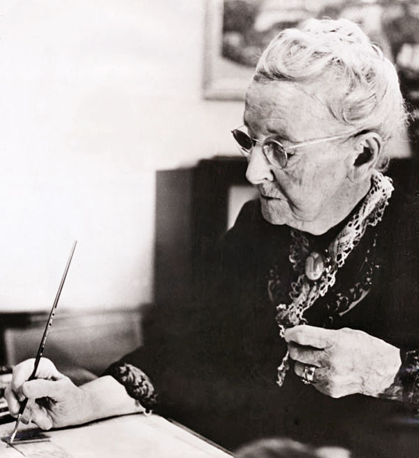 Grandma Moses with paintbrush working at a desk