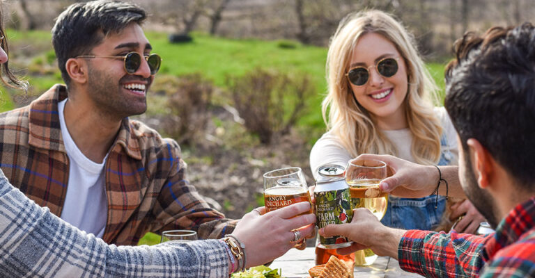 three friends outdoors toasting with glasses of cider