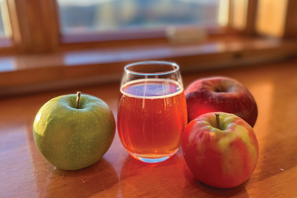 glass of cider and three apples on a table