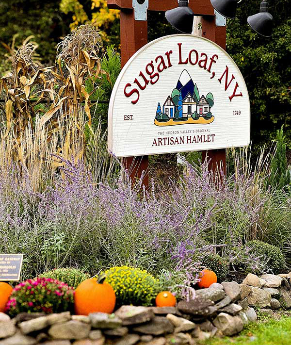 Sugarloaf Village sign with rock wall, pumpkins and plants