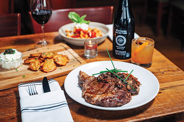 Plate of steak and side dishes with bottle of wine on a wooden table