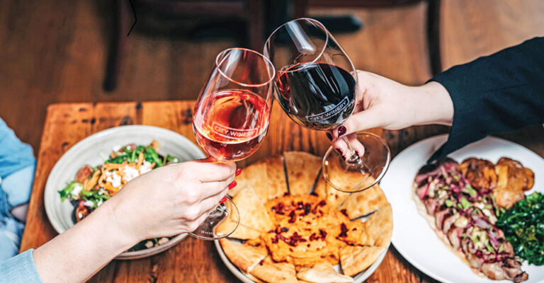 two wine glasses clinking over plates of food