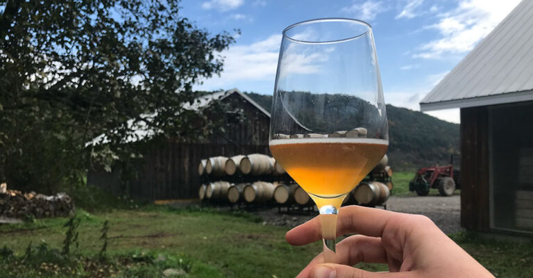 glass of cider up close with farm house in background