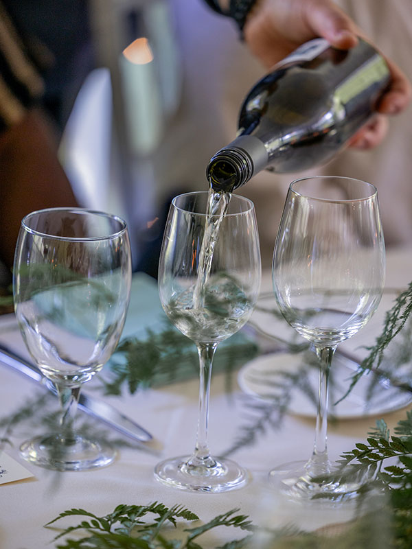 closeup of greene wine bottle pouring white wine into glasses on table
