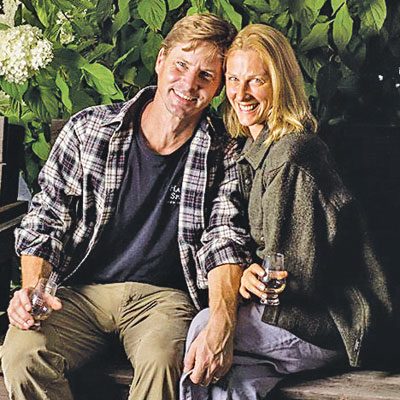 owner of HArvest Spirits with his wife seated on wood bench